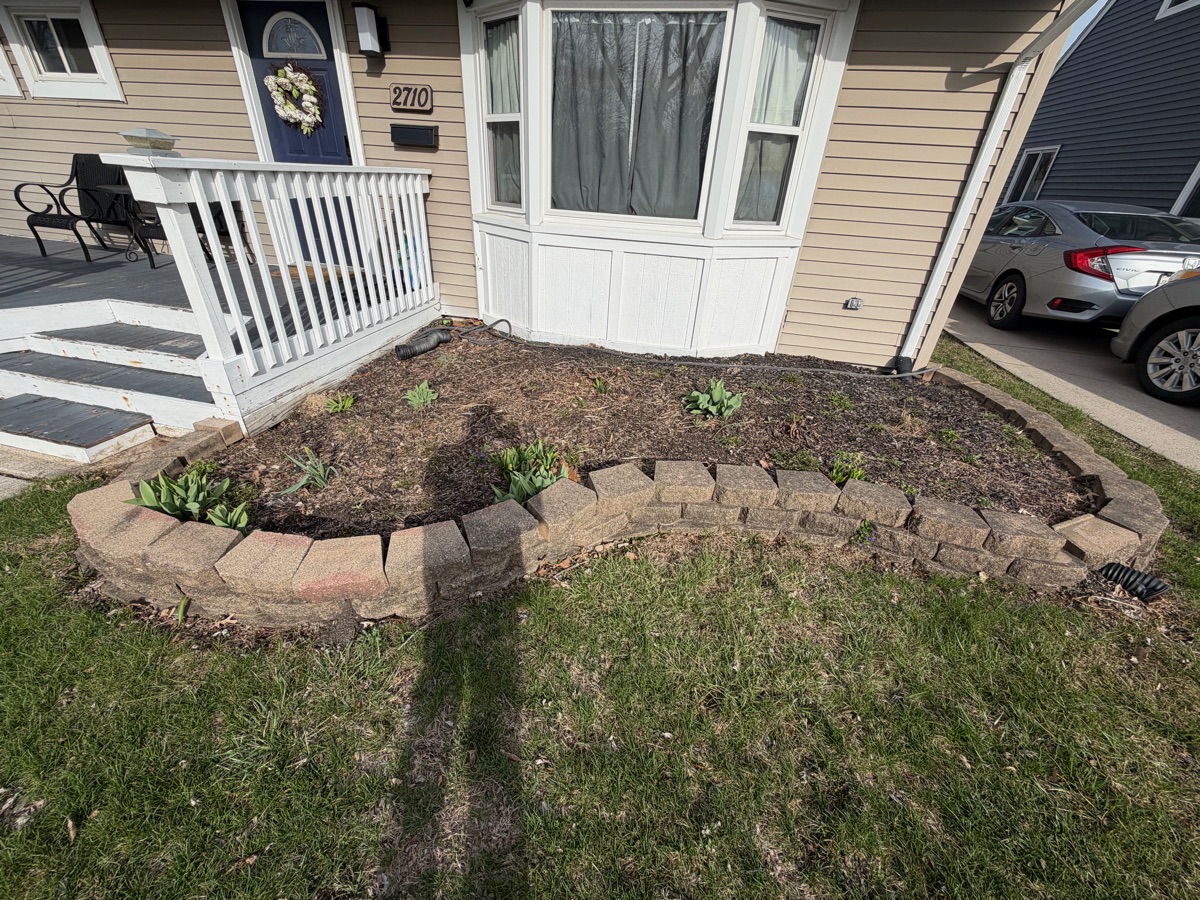 Before: bare front bed with stone retaining wall
